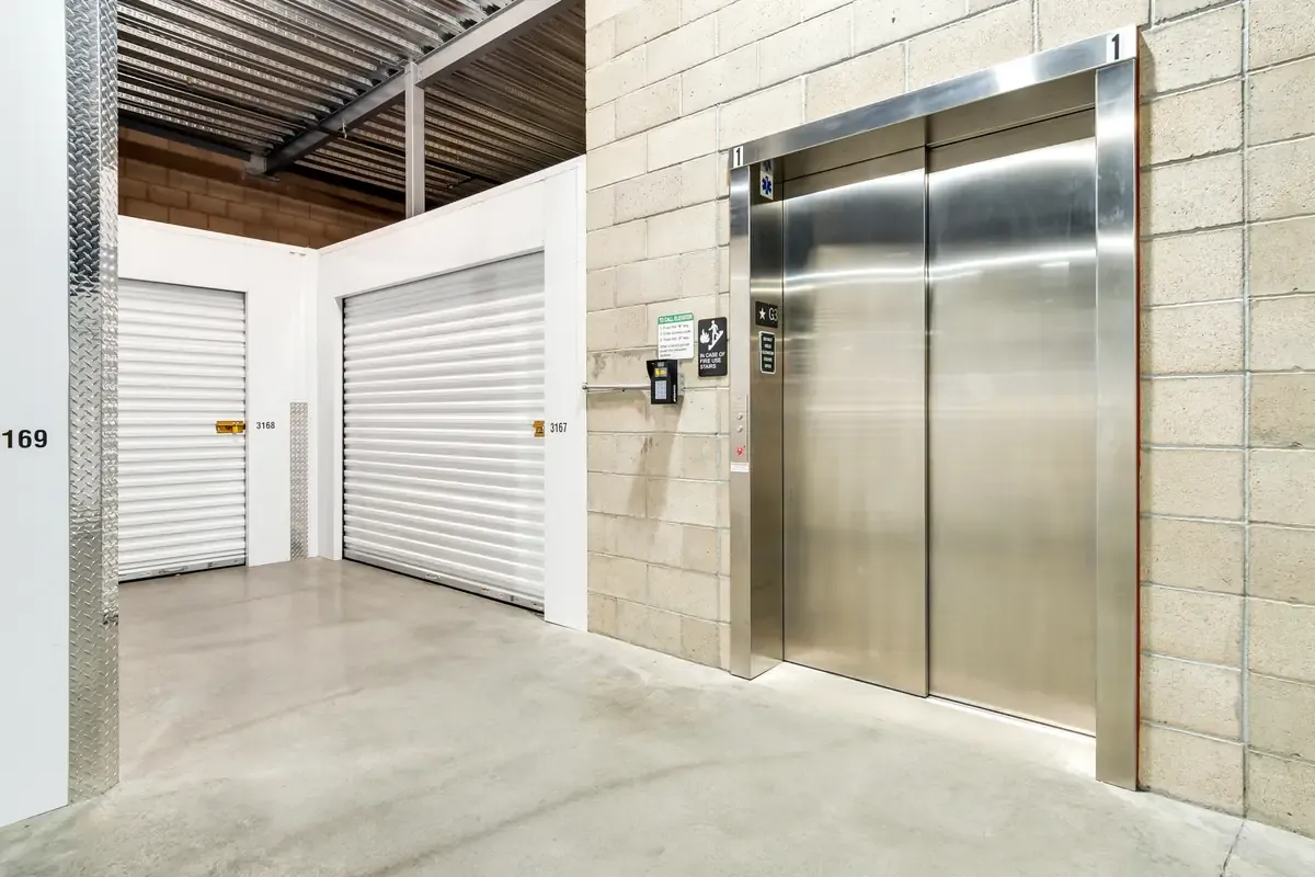 Stainless steel elevator in an indoor self-storage facility adjacent to a white storage unit door.