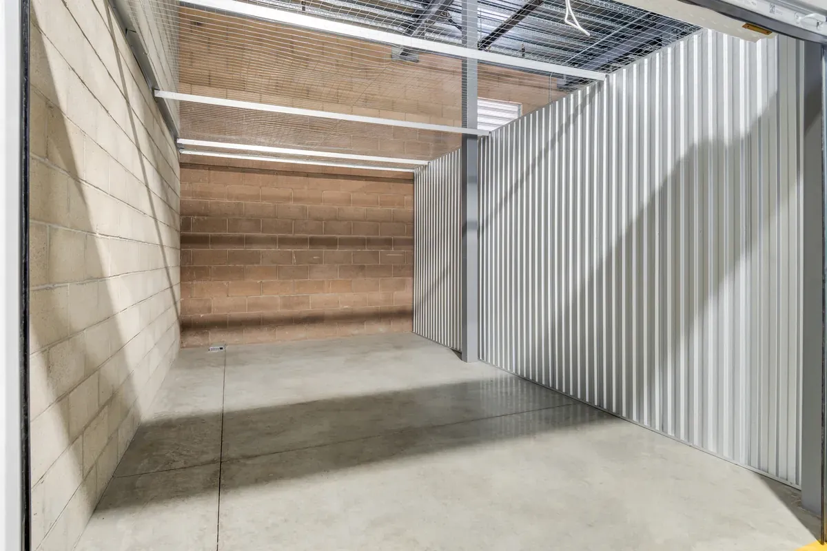 Interior of a large, empty self-storage unit with white metal walls and a brick back wall.