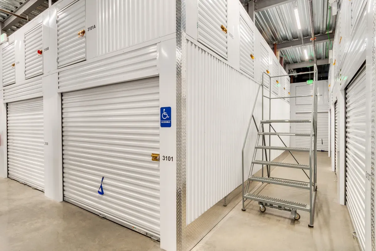 Indoor self-storage units with white roll-up doors, upper-tier lockers, and a rolling safety ladder.