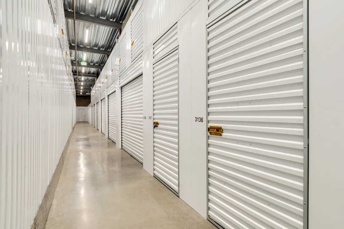Row of indoor climate-controlled self-storage units with white roll-up doors and polished concrete floor.